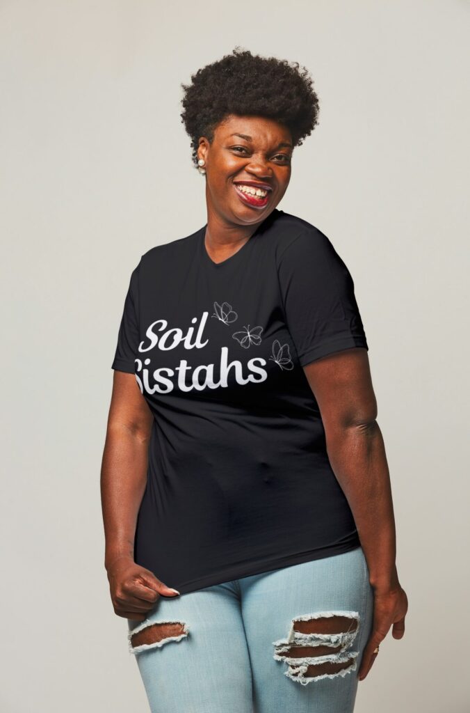 African-American woman wearing a black t-shirt with a delicate butterfly design and the term "soil sistahs" in script with ripped blue jeans.